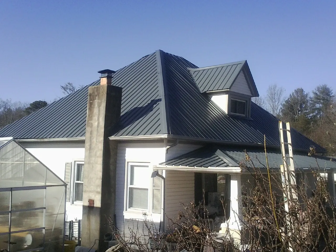 Dark blue standing seam metal roof on a white farmhouse with dormer — Slate & Tile Roof Repair by Roofing Brothers in North Garden