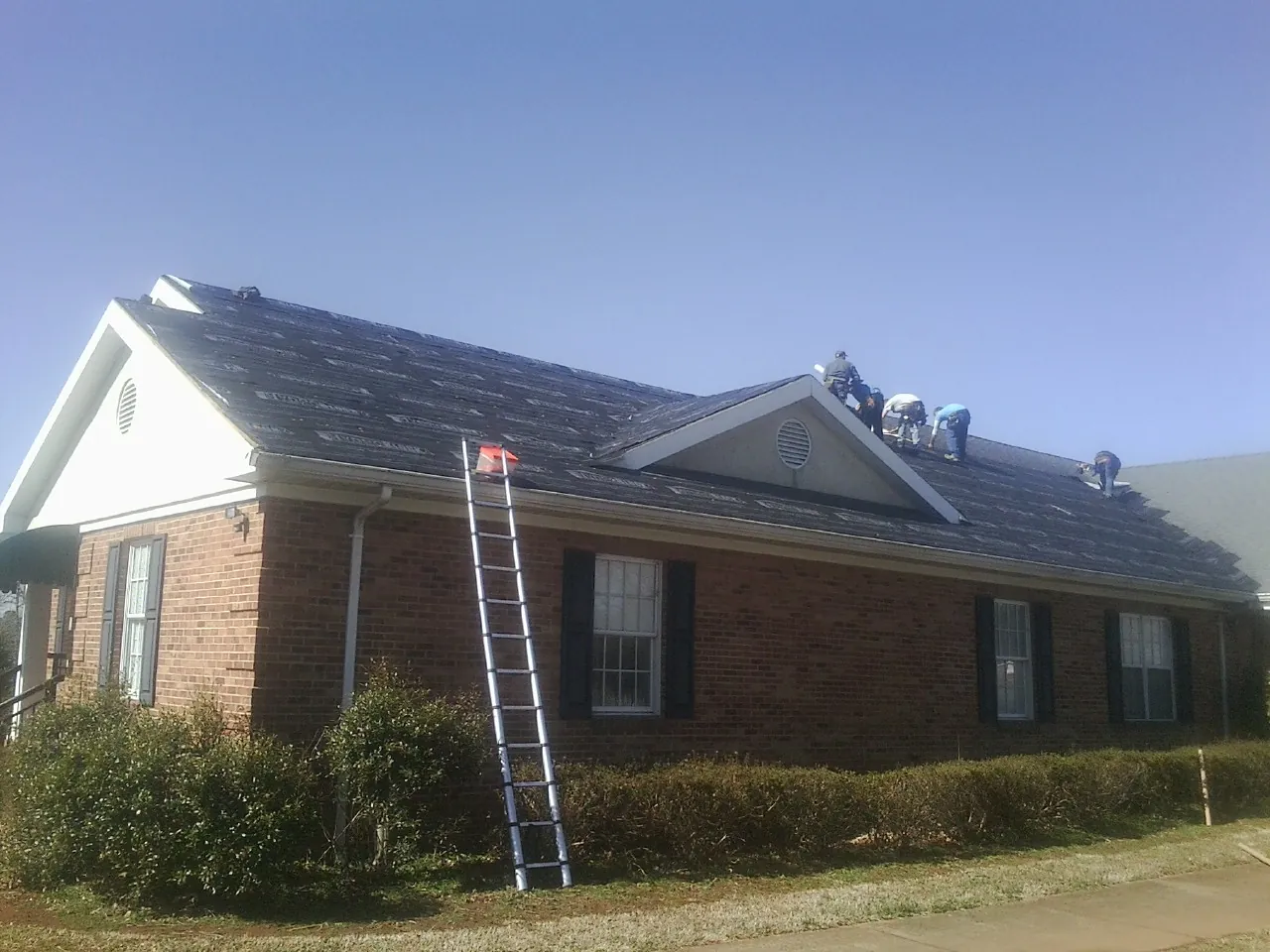 Crew tearing shingles off a brick ranch roof with a ladder set — Emergency Roof Repair work by our crew in North Garden