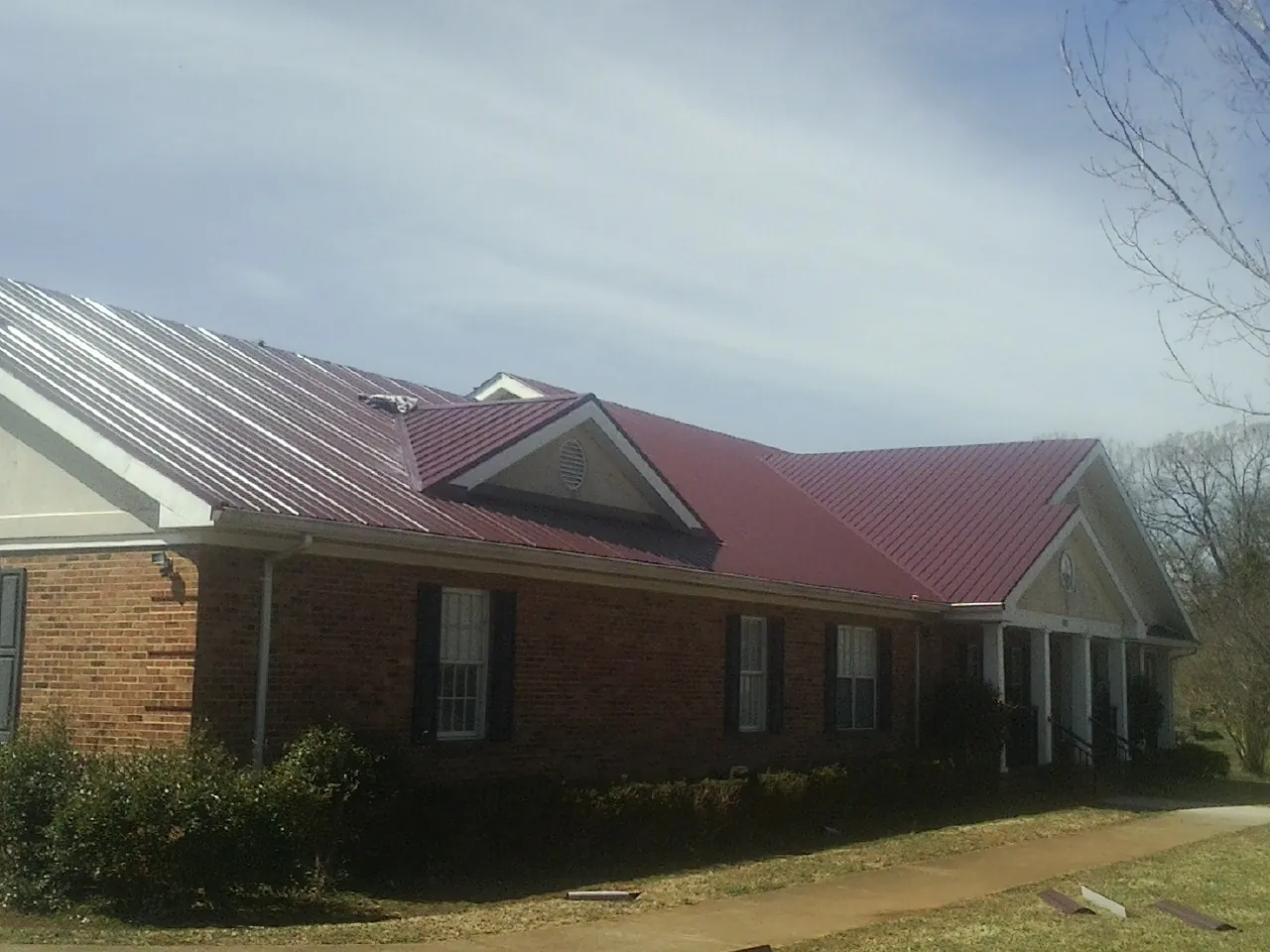Red metal roof with gabled entries on a long brick building, from a Hail Damage Roof Repair job in North Garden