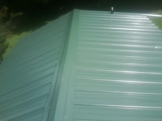 New green metal panels meeting at the ridge of a roof — Flat Roof Repair work by our crew in North Garden