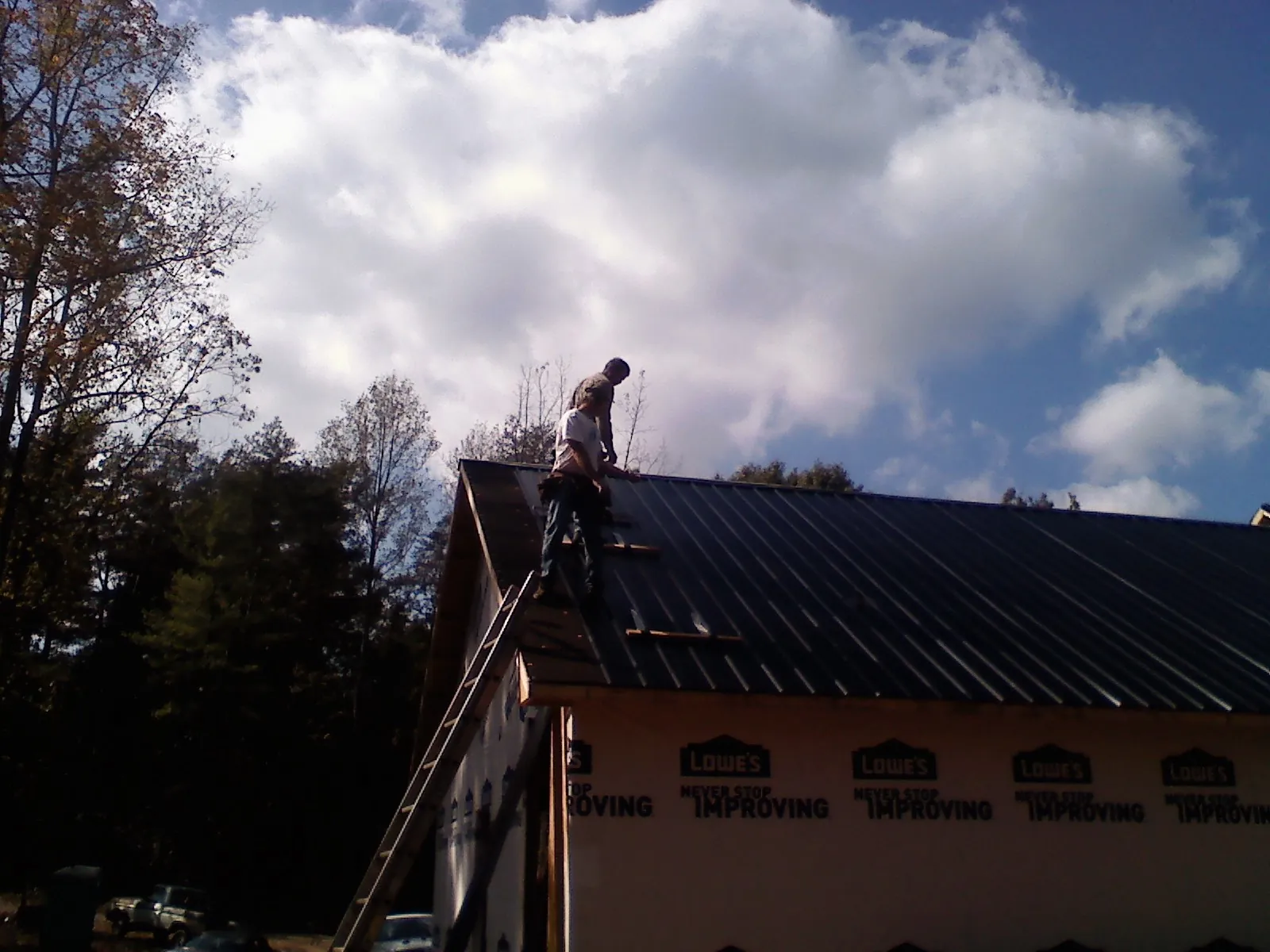 Roofer fastening dark metal panels high against a cloudy sky, from a Roof Inspection job in North Garden