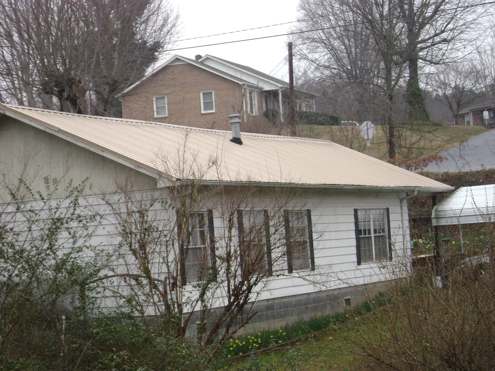 Tan metal roof on a white sided house set into a hillside — Commercial Roofing by Roofing Brothers in North Garden